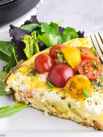 A wedge of smoked salmon spinach frittata garnished with cherry tomatoes.