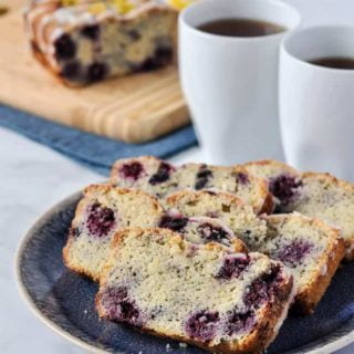 Slices of Keto blackberry bread on a blue plate with two coffee cups in the background.