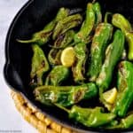 Blistered Shishito Peppers in a cast-iron skillet with lemon slices