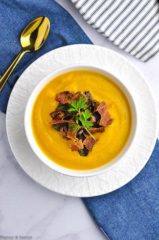 A bowl of soup with toasted sage leaves, crispy shallots, crumbled bacon and herbs.