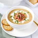 A bowl of Potato Leek Soup with crackers and a spoon.
