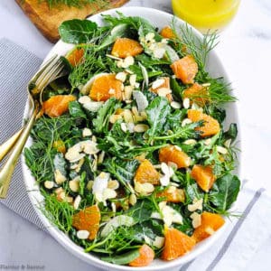 Overhead view of Kale and Cara Cara Orange Salad in a white oval bowl with dressing in the background.