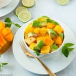 Mango Avocado Chili Lime Salad in a white bowl garnished with lime slices and mint leaves.