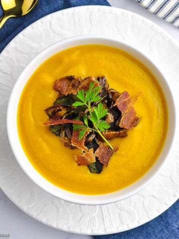 Overhead image of a bowl of Butternut Squash Soup in a white bowl on a blue cloth