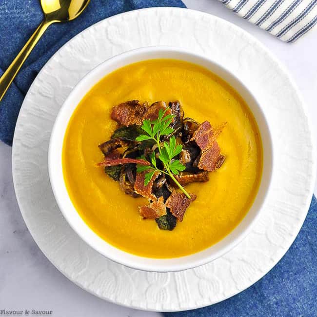 Overhead image of a bowl of Butternut Squash Soup in a white bowl on a blue cloth