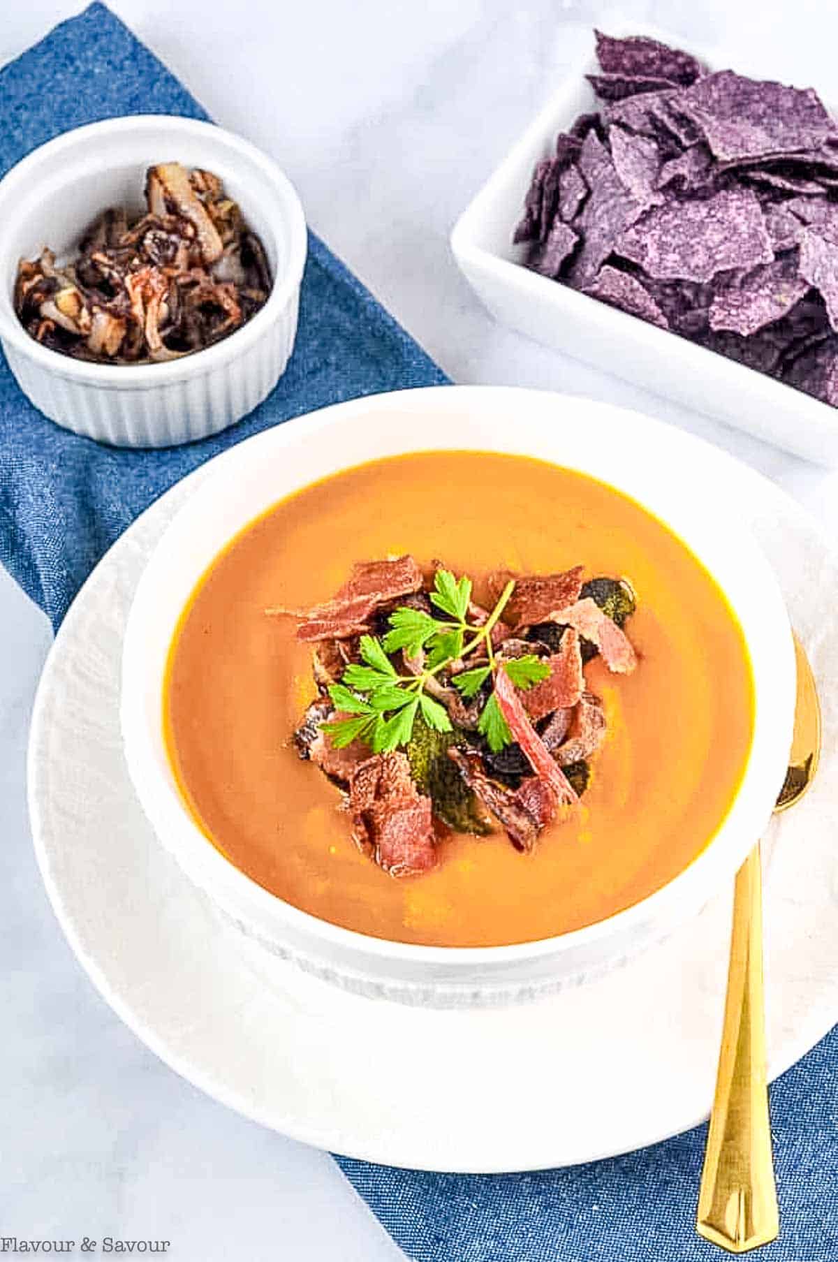 A white bowl with butternut squash soup with a small bowl of crispy shallots beside.