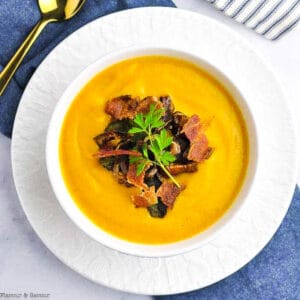 Overhead image of a white bowl of butternut squash soup with ginger and orange garnished with crispy fried shallots.