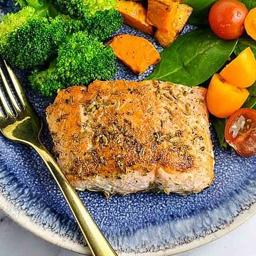 A fennel crusted salmon fillet on a plate with roasted vegetables.