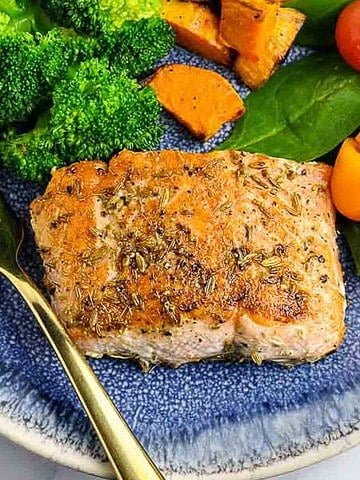 A fennel crusted salmon fillet on a plate with roasted vegetables.