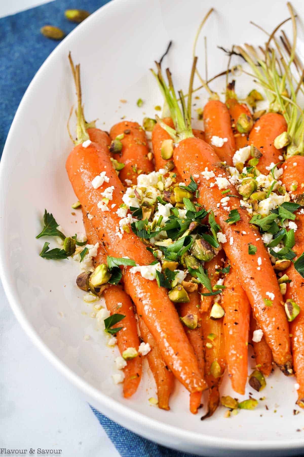 Oven roasted carrots in a white oval dish topped with feta cheese, pistachios and parsley.