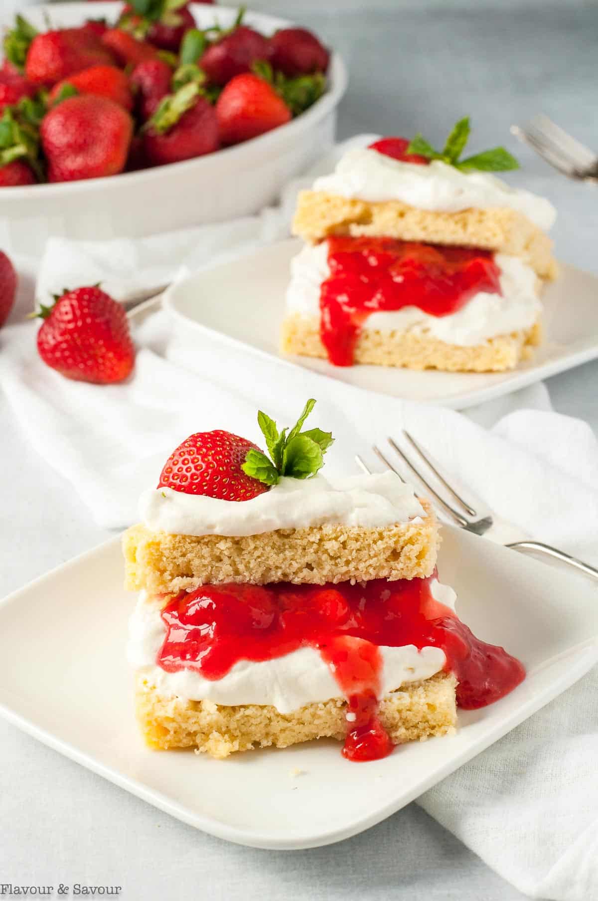 Two servings of Keto Strawberry Shortcake with a bowl of strawberries in the background.
