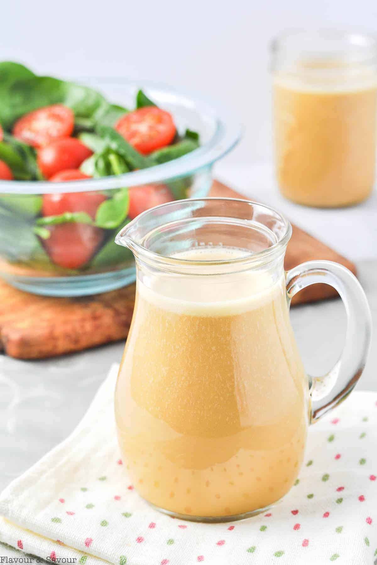 a small pitcher of Hollyhock Nutritional Yeast Dressing with a salad in the bacground