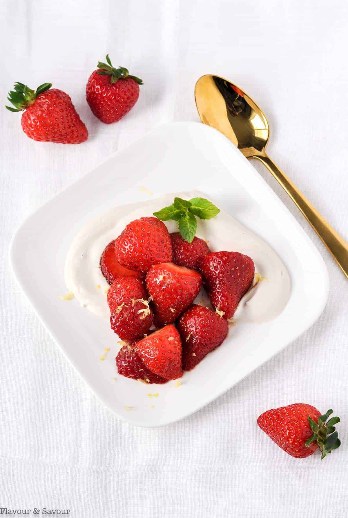 Macerated Strawberries with Cashew Cream on a plate with a gold spoon beside.