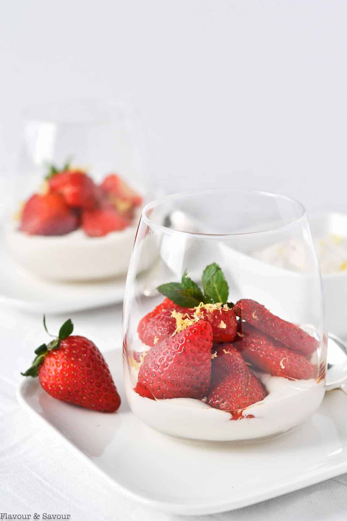 Two dessert glasses with cashew cream topped with macerated strawberries.