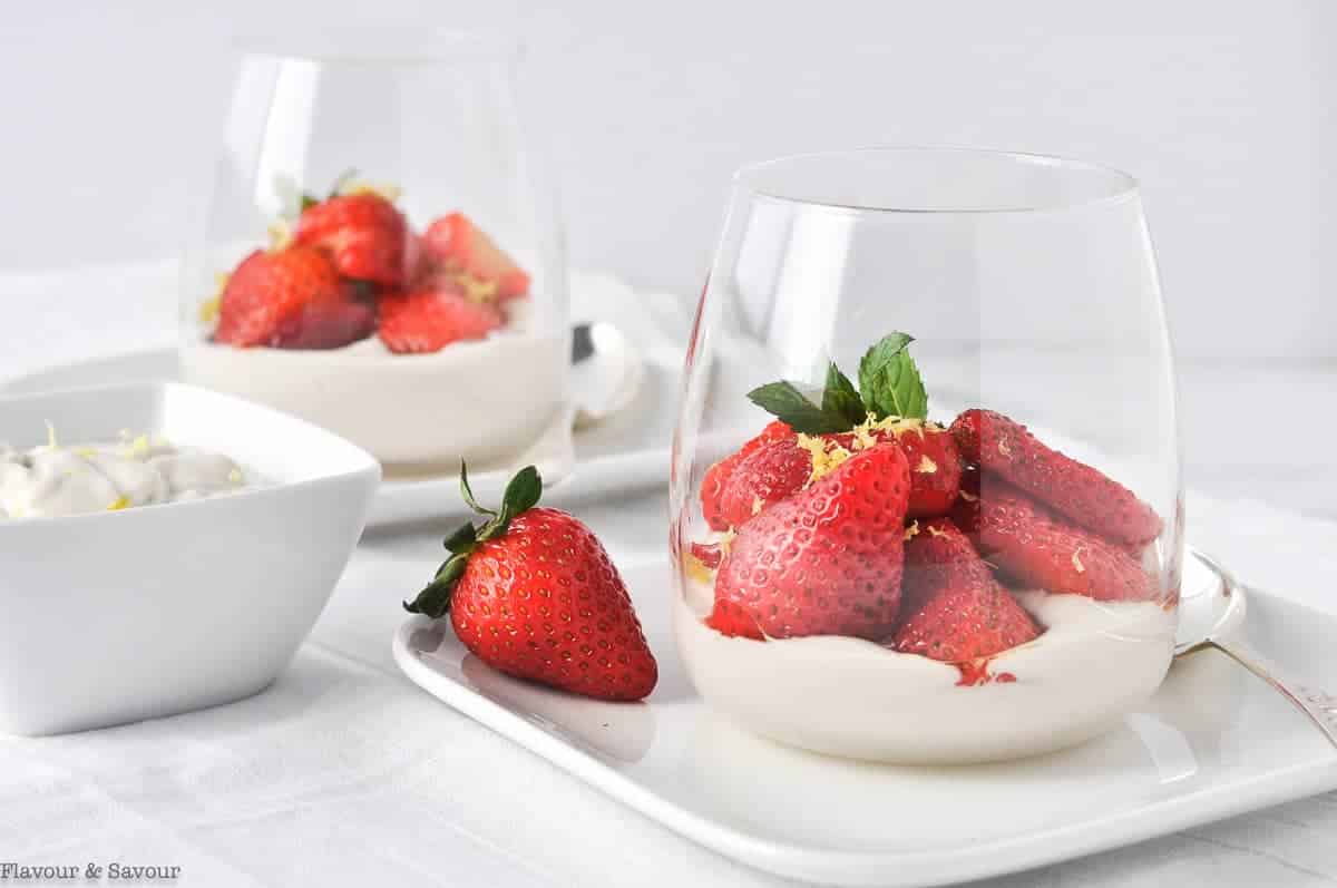 Macerated sliced strawberries in clear dessert glasses with a small bowl of cashew cream beside.