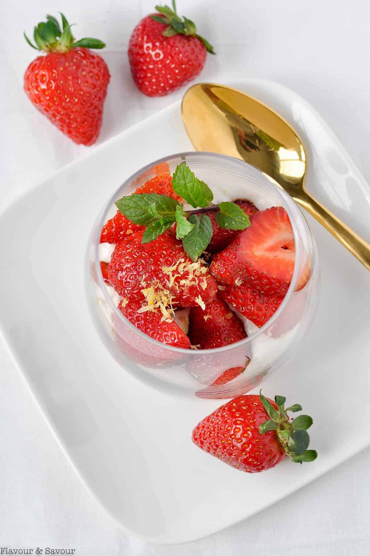 Overhead view of macerated strawberries with cashew cream garnished with lemon zest and a sprig of mint.