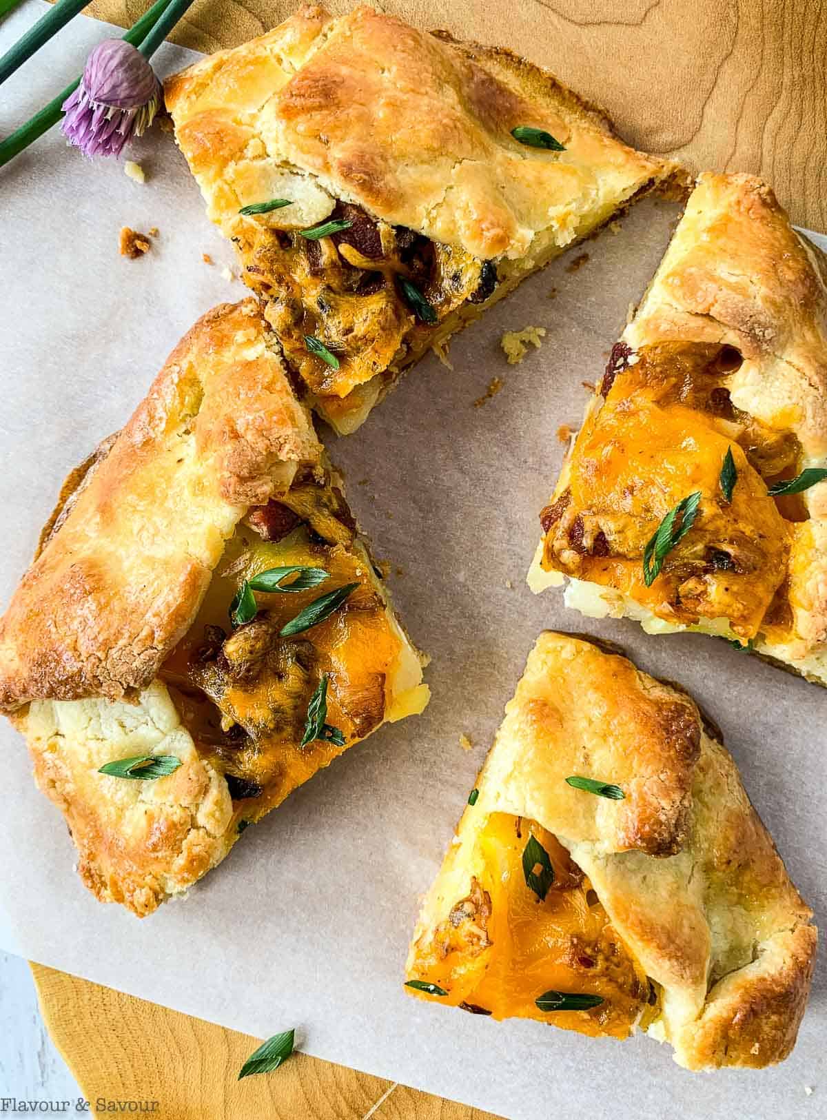 Four wedges of Potato Galette with Bacon and Cheese on a wooden board with fresh chive flowers on the side.