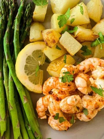 Shrimp with lemon garlic butter, asparagus spears an roasted potatoes on a dinner plate.