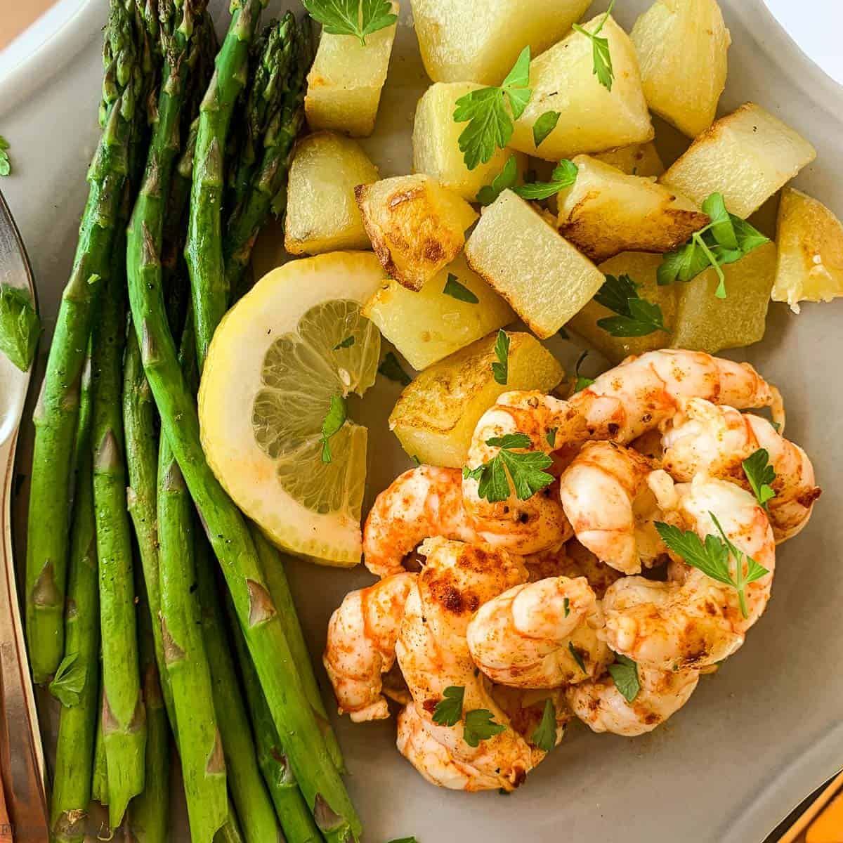 Close up view of Sheet Pan Lemon Garlic Prawns, asparagus and roast potatoes on a plate.