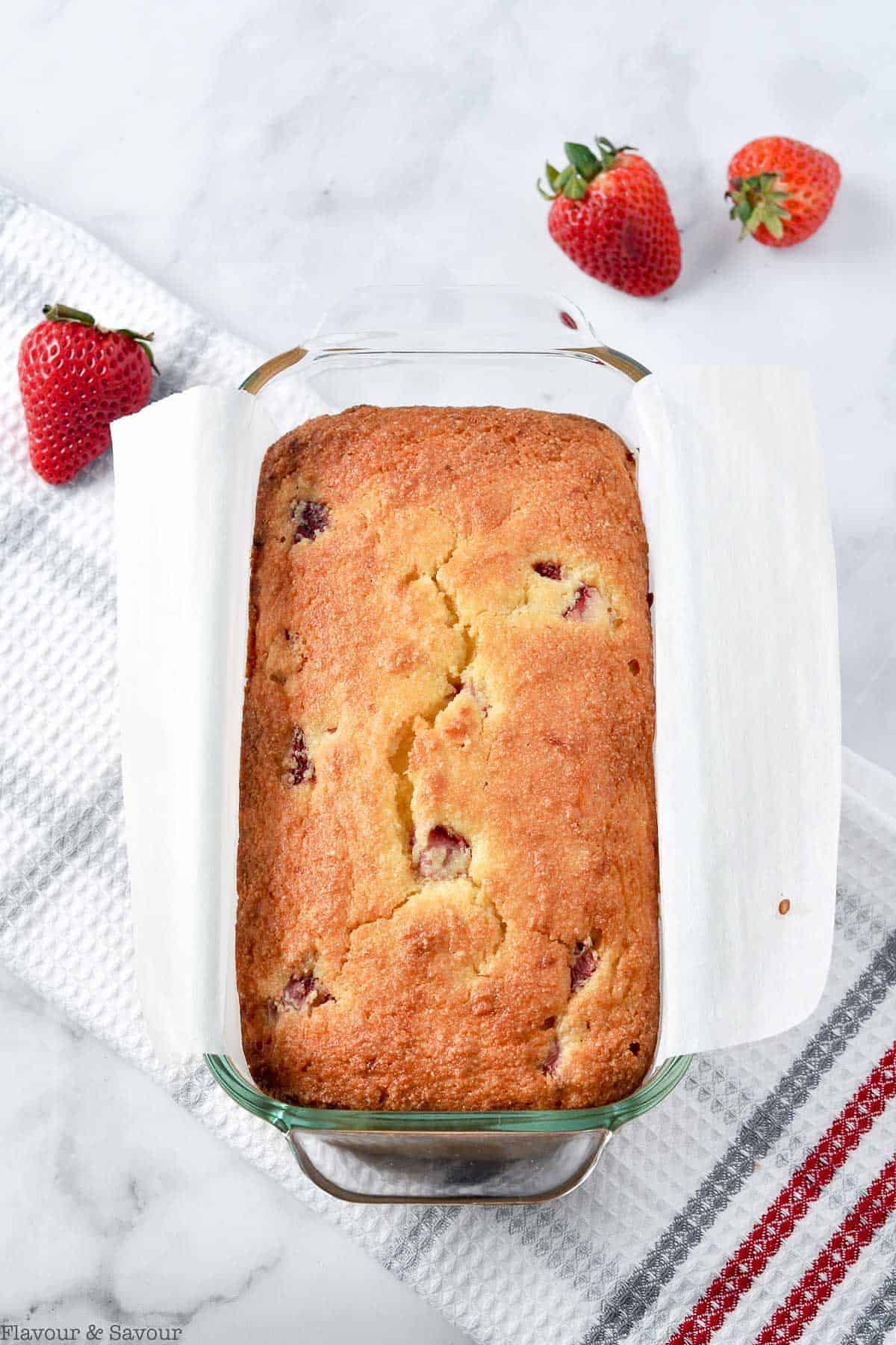 Baked Strawberry Lemon Loaf in a loaf pan with fresh strawberries on the counter.