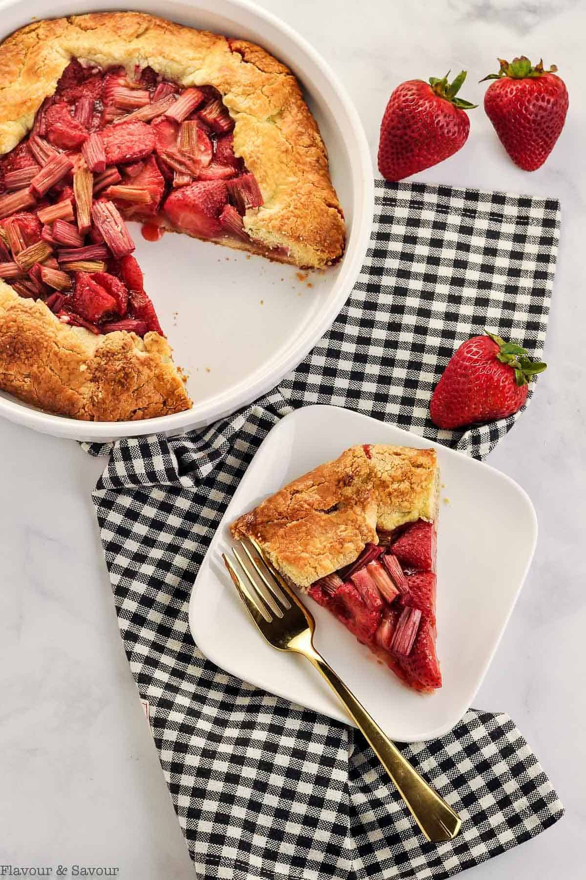 Overhead view of strawberry rhubarb galette on a black checkered cloth.