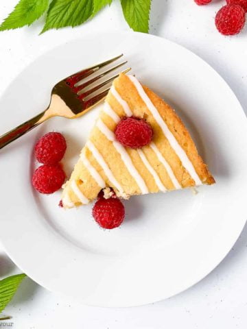 A slice of flourless Raspberry Lemon Ricotta Cake with fresh raspberries and raspberry leaves