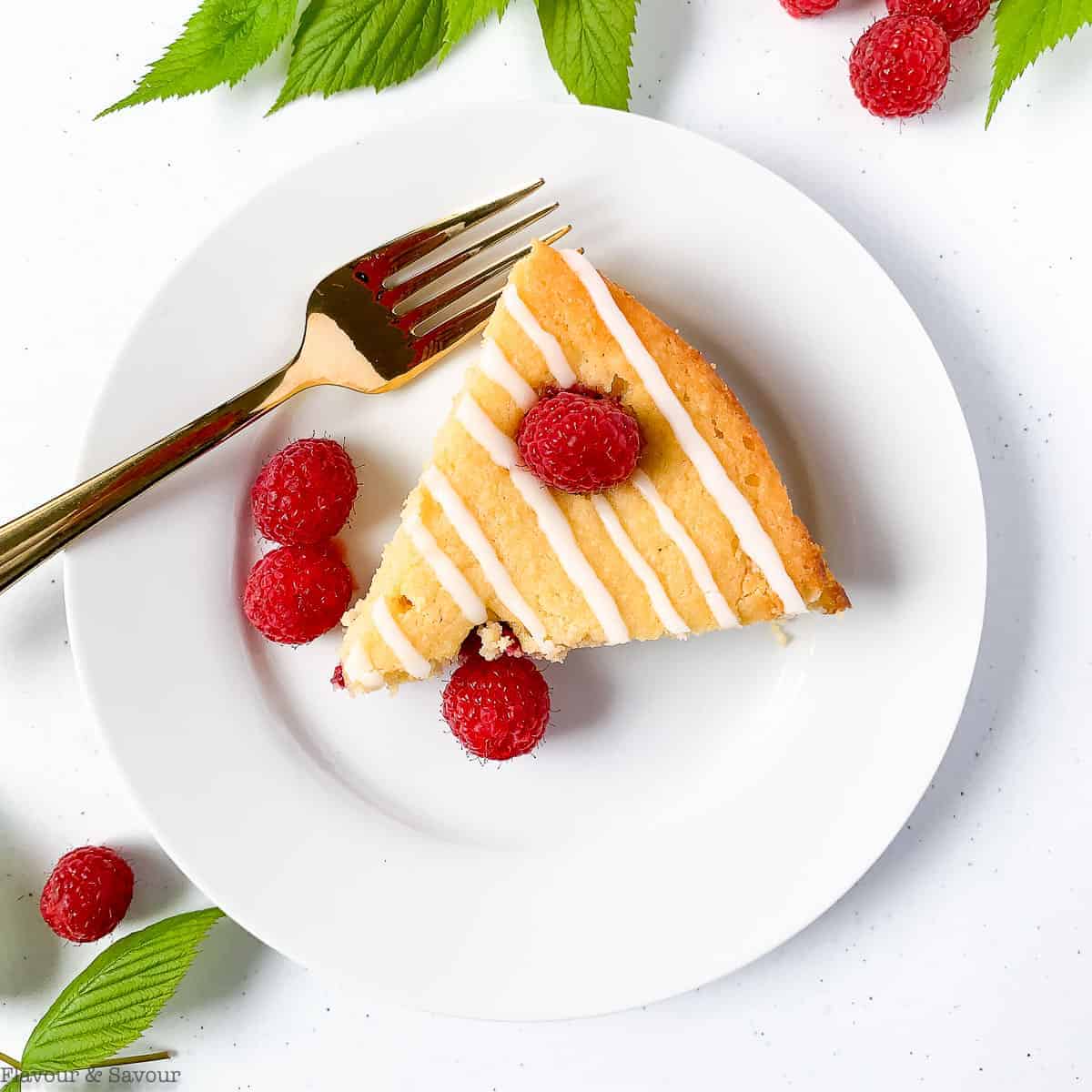 A slice of Raspberry Lemon Ricotta Cake on a white round plate with fresh berries and raspberry leaves