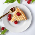 A slice of Flourless Raspberry Lemon Ricotta Cake with fresh raspberries and raspberry leaves