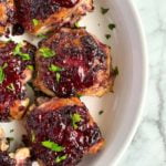 Blackberry Glazed Chicken Thighs in a white round serving dish sprinkled with fresh parsley