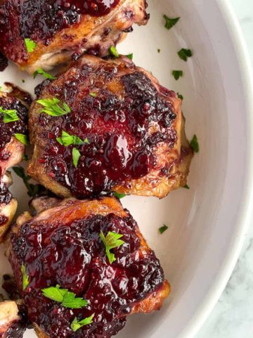 Blackberry Glazed Chicken Thighs in a white round serving dish sprinkled with fresh parsley