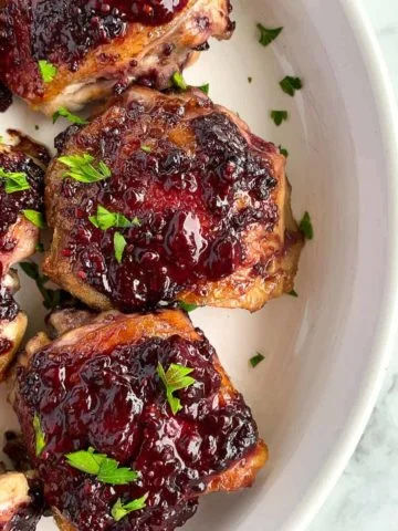 Blackberry Glazed Chicken Thighs in a white round serving dish sprinkled with fresh parsley