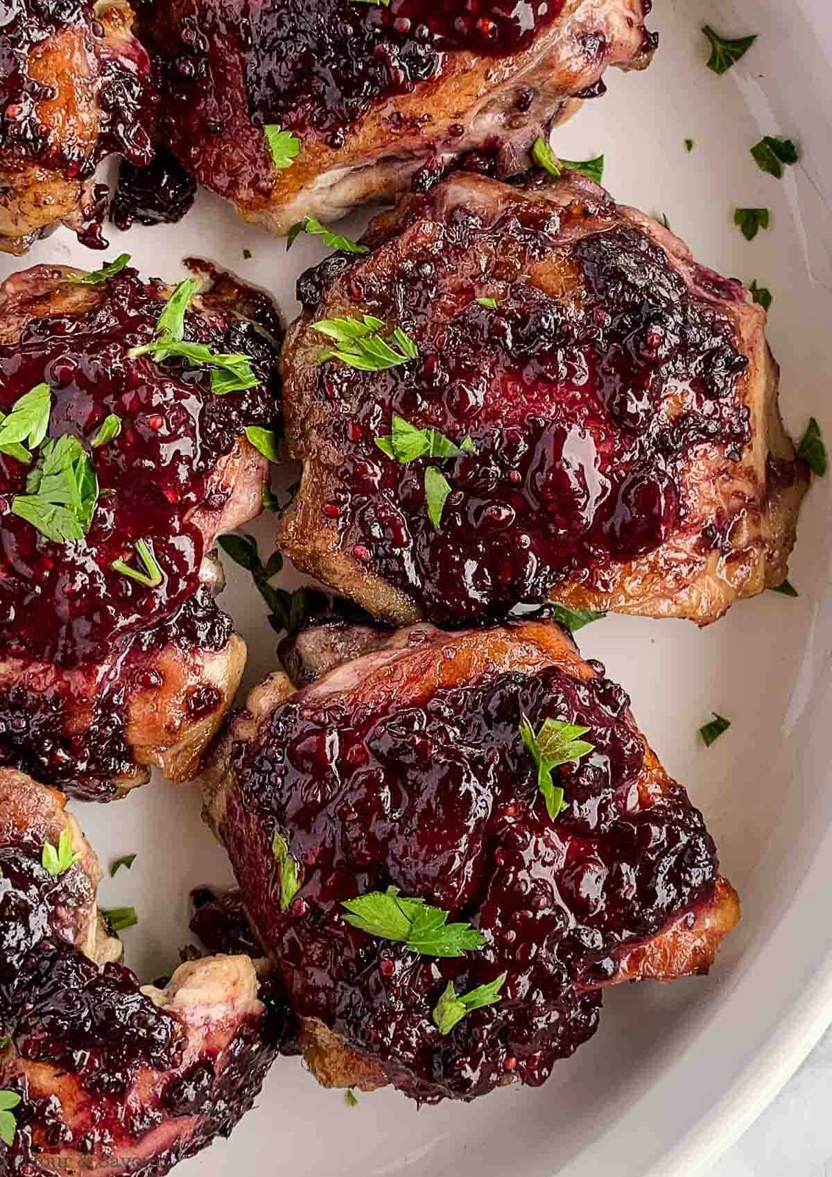 Close up view of Blackberry Glazed Chicken thighs in a white serving dish garnished with fresh parsley.