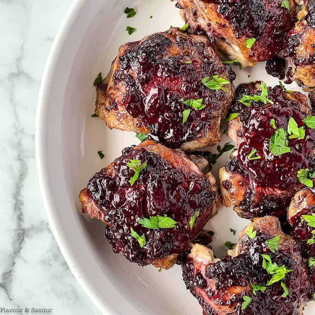 blackberry glazed chicken thighs in a serving dish with fresh parsley