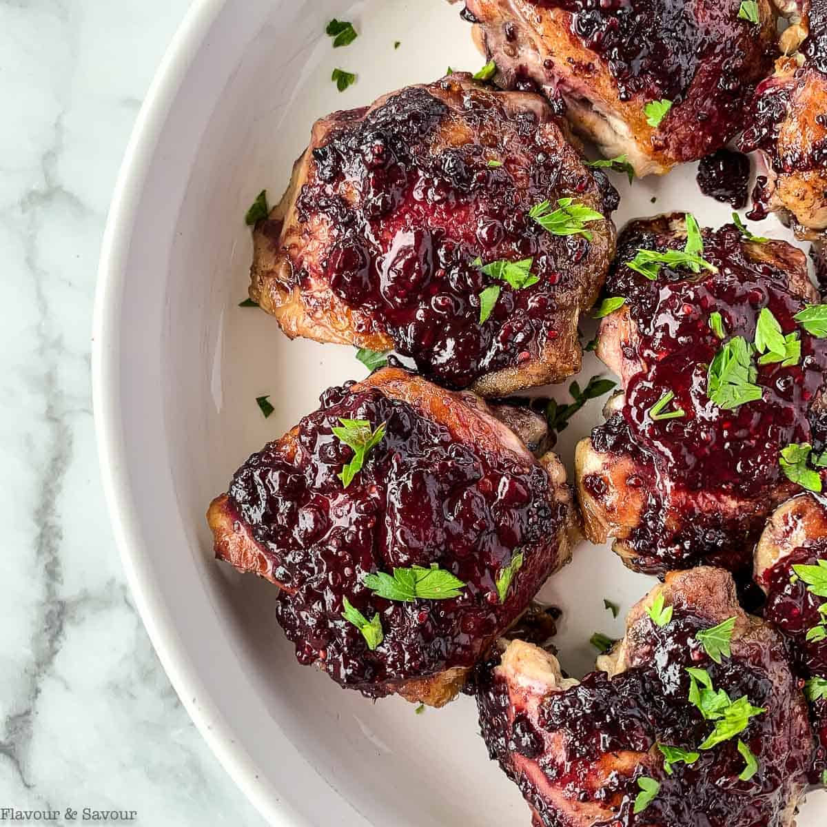 Blackberry glazed chicken thighs in a serving dish with fresh parsley.
