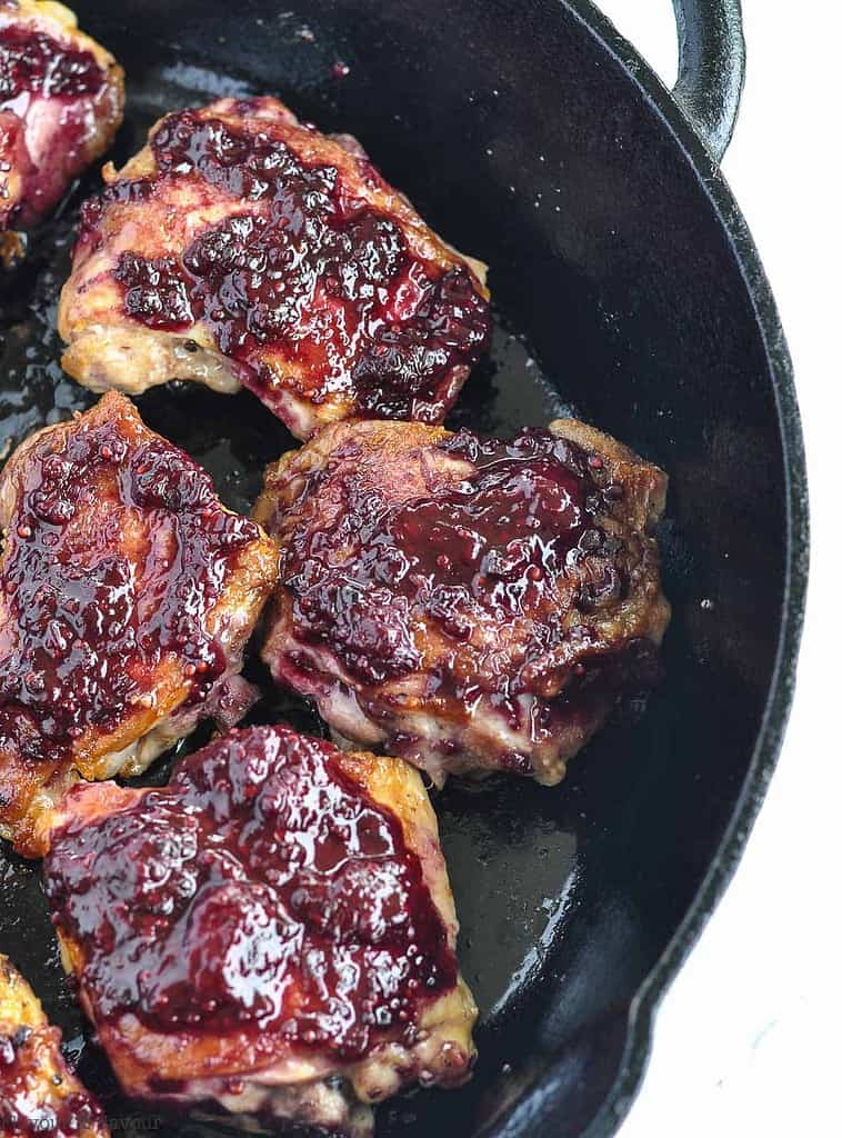 overhead view of chicken thighs brushed with blackberry glaze in a cast iron pan