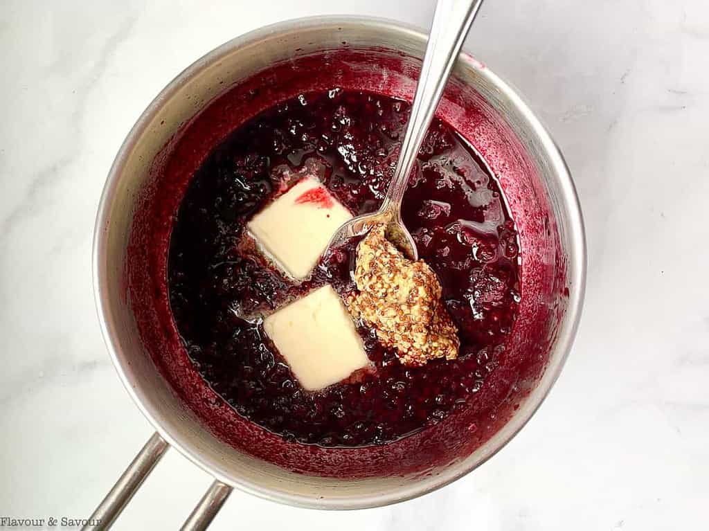 Adding butter and whole-grain mustard to reduced blackberry sauce in a saucepan