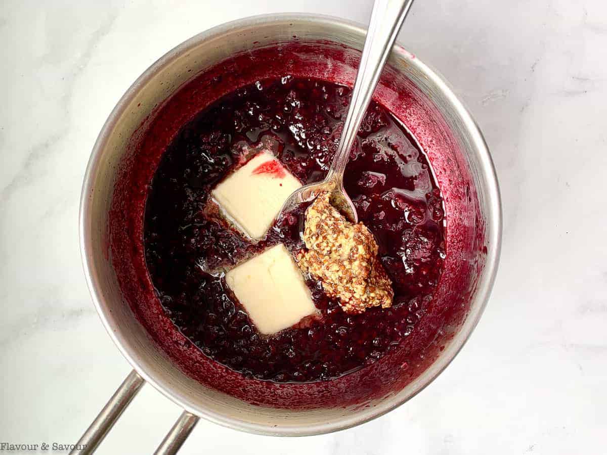 Adding butter and whole-grain mustard to reduced blackberry sauce in a saucepan.