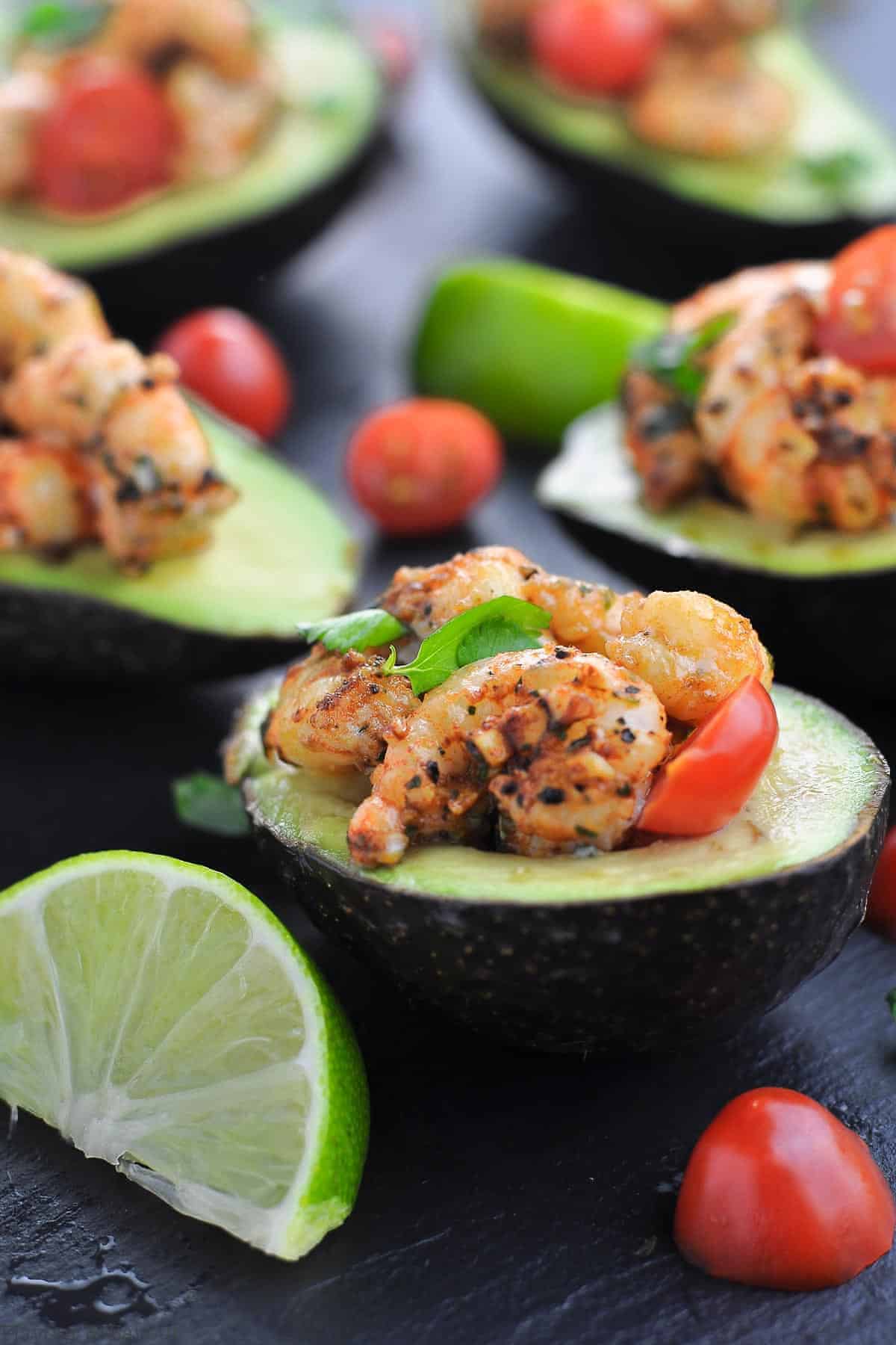 Cajun Shrimp Stuffed Avocados with quartered limes on a black tray