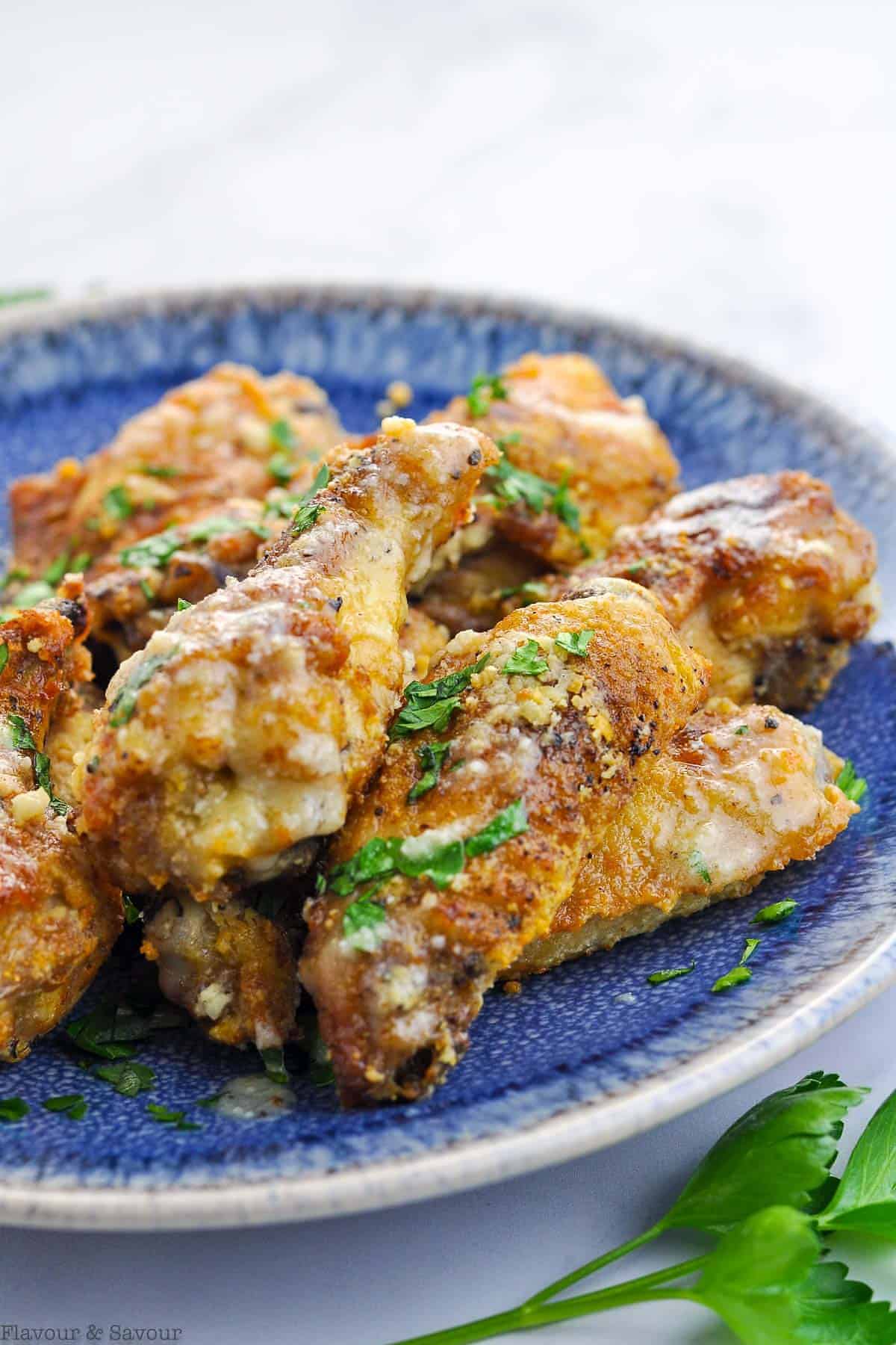 Close up view of Garlic Parmesan Air Fryer Wings sprinkled with fresh parsley on a blue plate