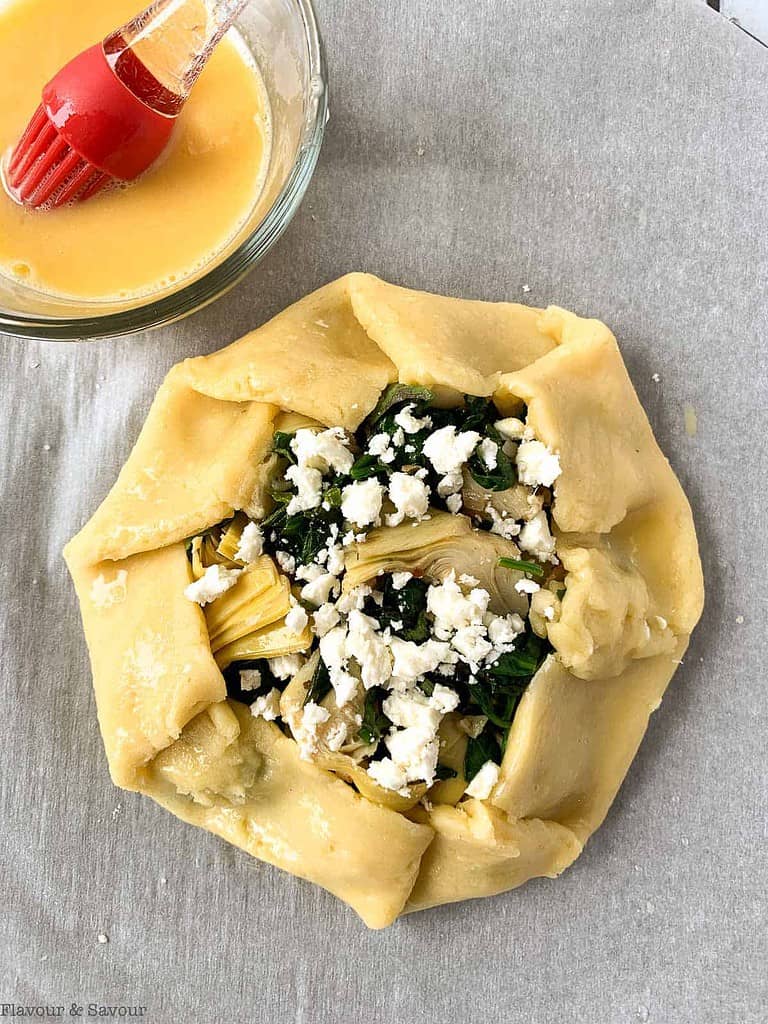 Brushing egg wash on spinach artichoke galette