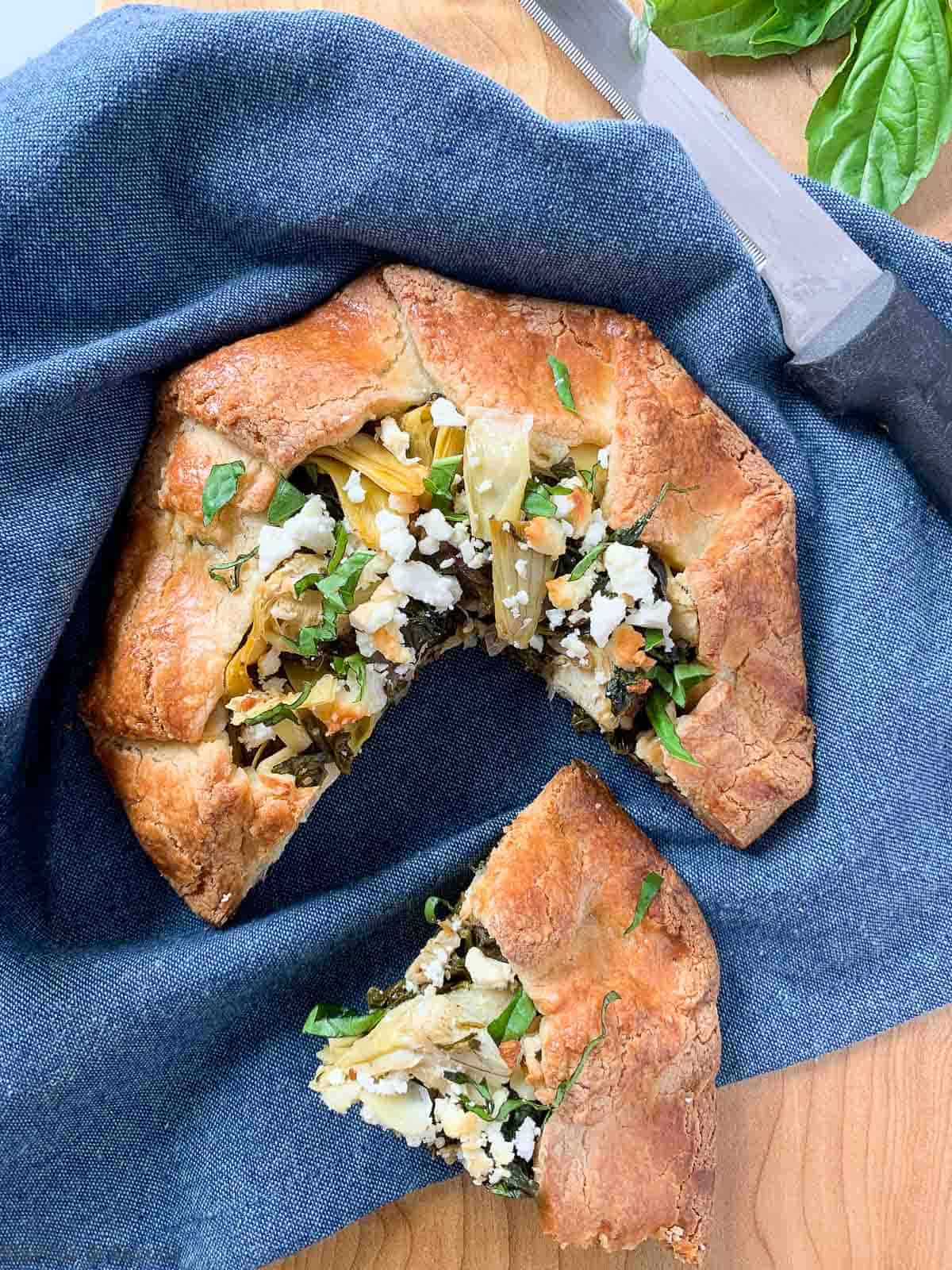 Gluten Free Spinach Artichoke Galette on a blue cloth with one wedge removed