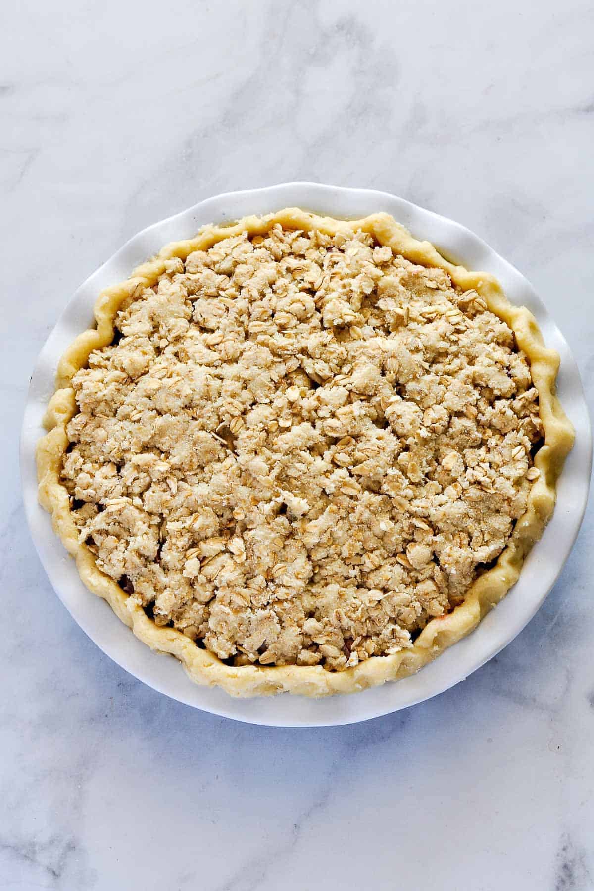 Adding oatmeal crumb topping to Strawberry Rhubarb Crumble Pie.