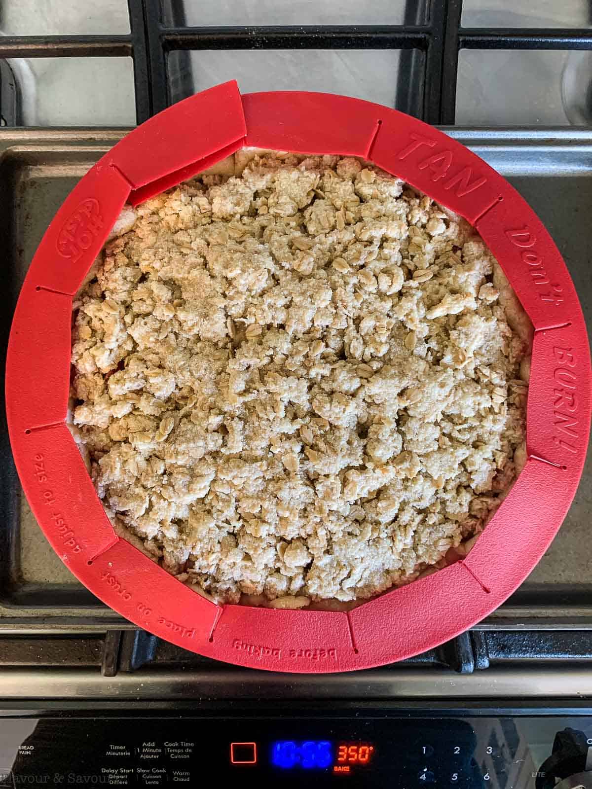 Placing a pie shield on an unbaked Strawberry Rhubarb Crumble Pie.