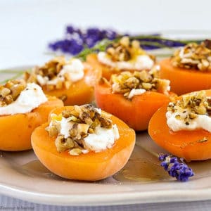 Fresh apricots on a gray plate topped with goat cheese, walnuts and honey with lavender sprigs