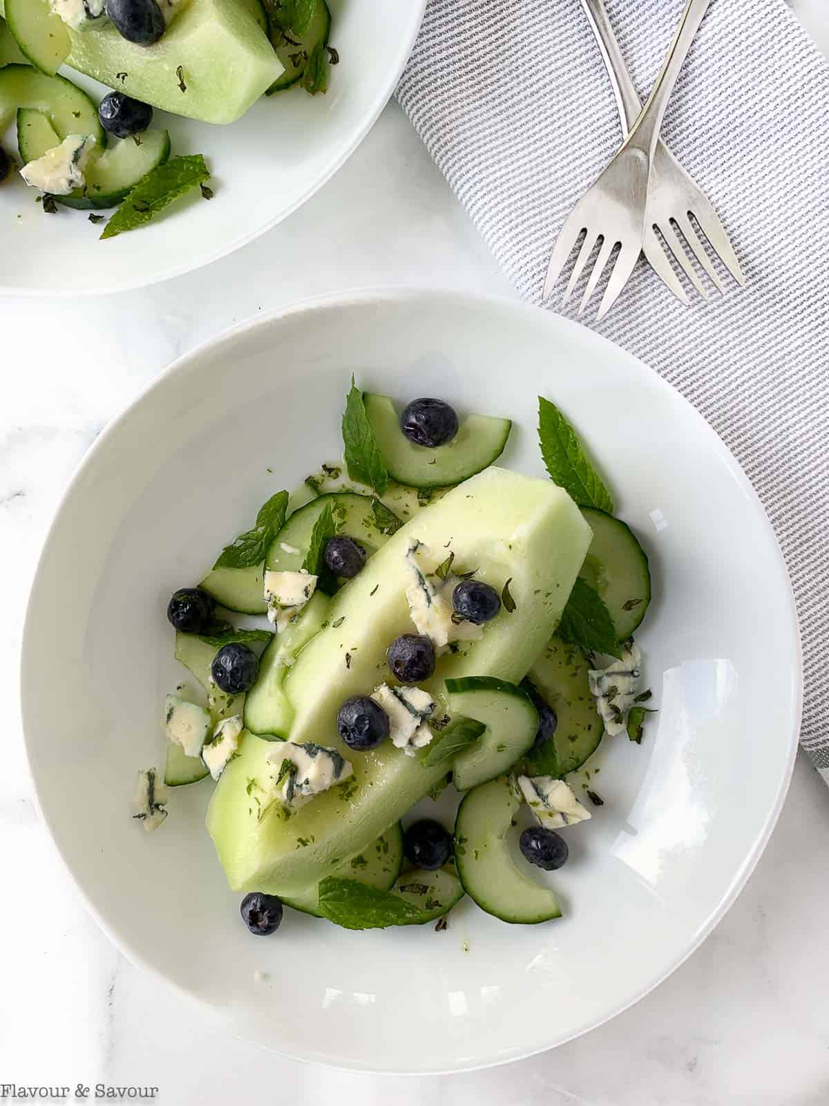 overhead view of Honeydew Melon Salad. A wedge of honeydew with blueberries, cucumbers, blue cheese and mint leaves.