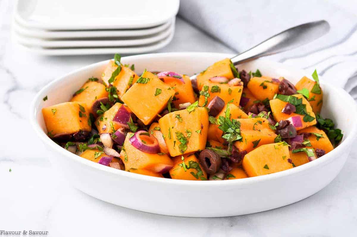 A bowl of Mediterranean Cantaloupe Salad with serving plates