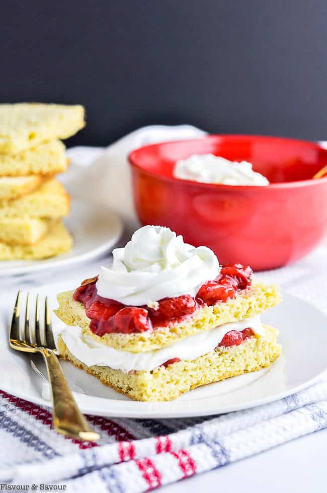 Sugar-Free Strawberry Shortcake topped with a red bowl of whipped cream in the background.