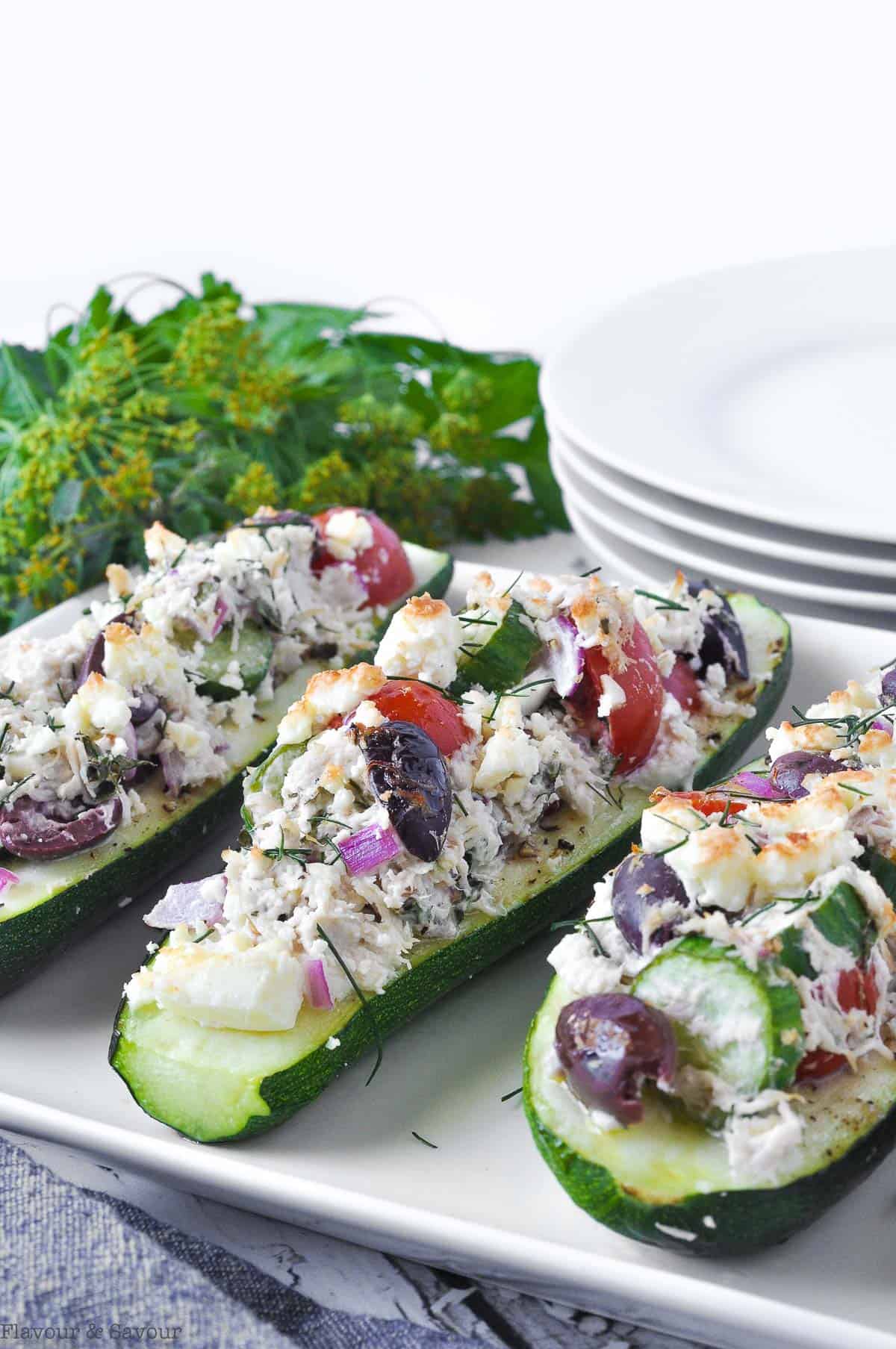 Baked Stuffed Zucchini Boats with Chicken and Feta on a serving plate with fresh herbs