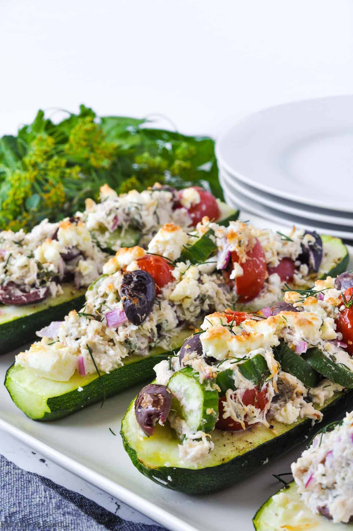 Greek Chicken Stuffed Zucchini Boats with herbs and plates in the background.