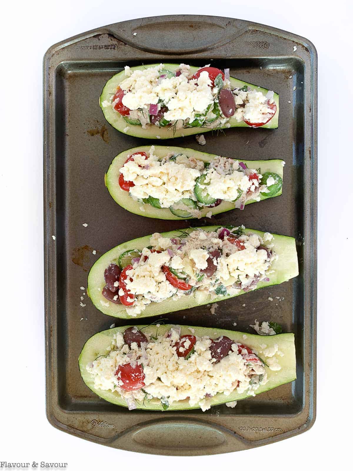 greek chicken stuffed zucchini boats on a baking sheet